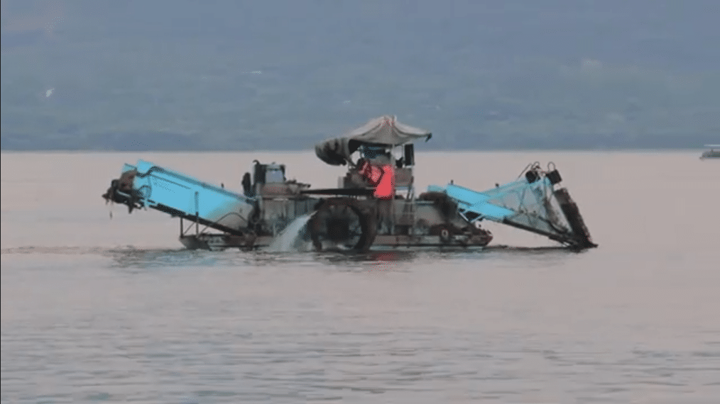 Un bateau nettoie une rivière victime de pollution plastique